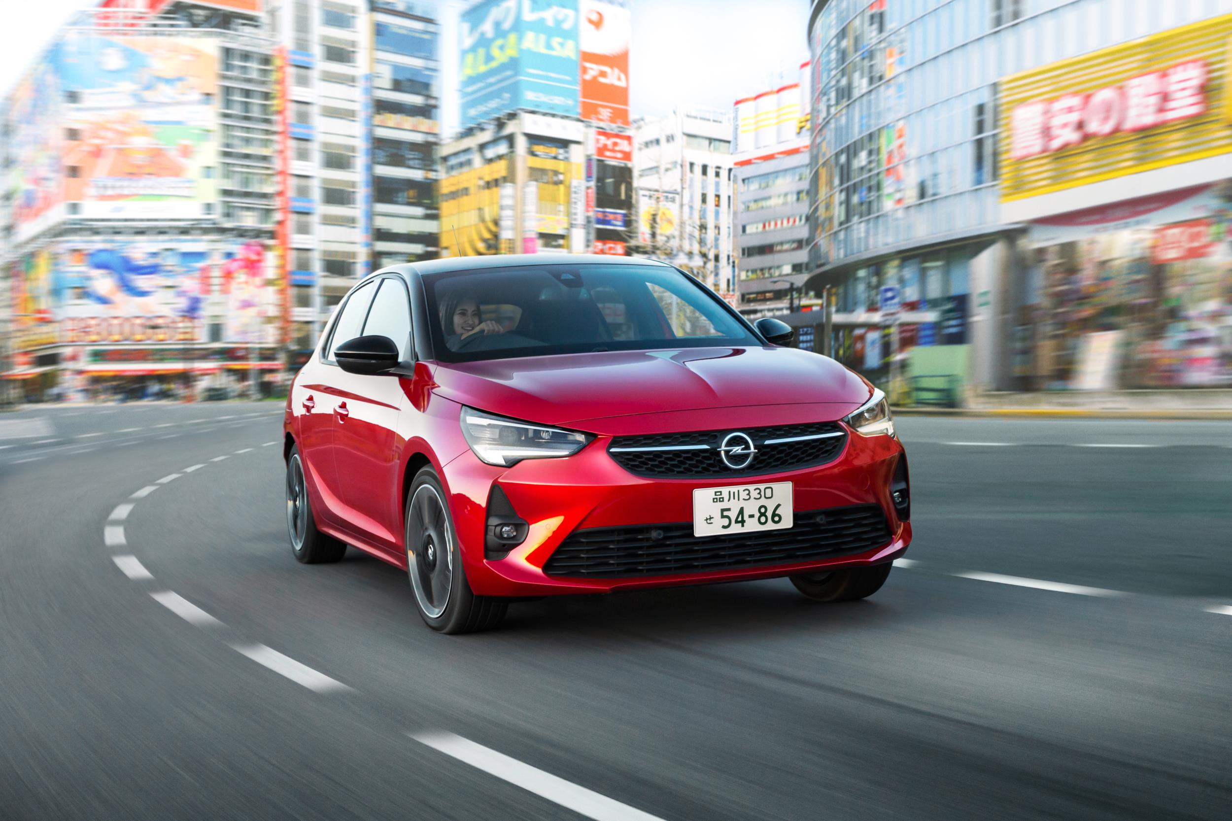 Un Opel Corsa rojo circulando por una calle de Japón